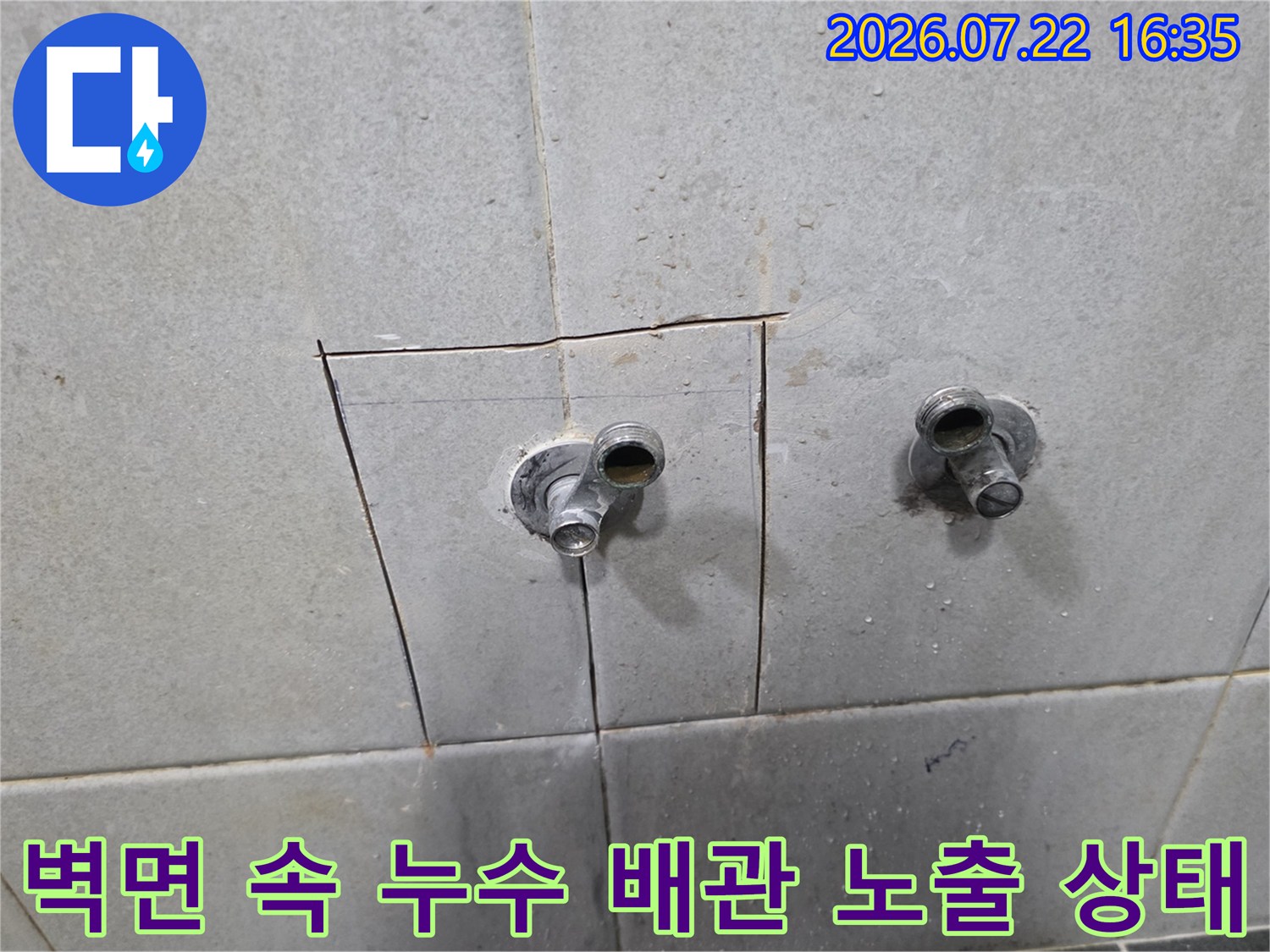 흰색 계열의 타일 벽면에 사각형으로 굴착된 구멍과 그 사이로 나온 수도 배관