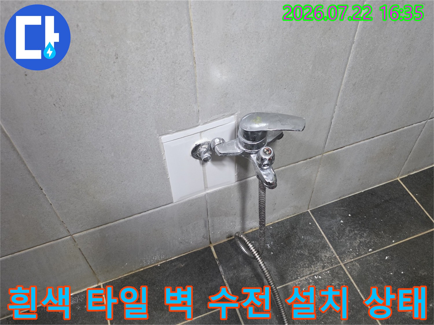 흰색 정사각형 타일 마감재 위에 부착된 금속 재질의 수도꼭지-하단에 호스가 연결되어 있음