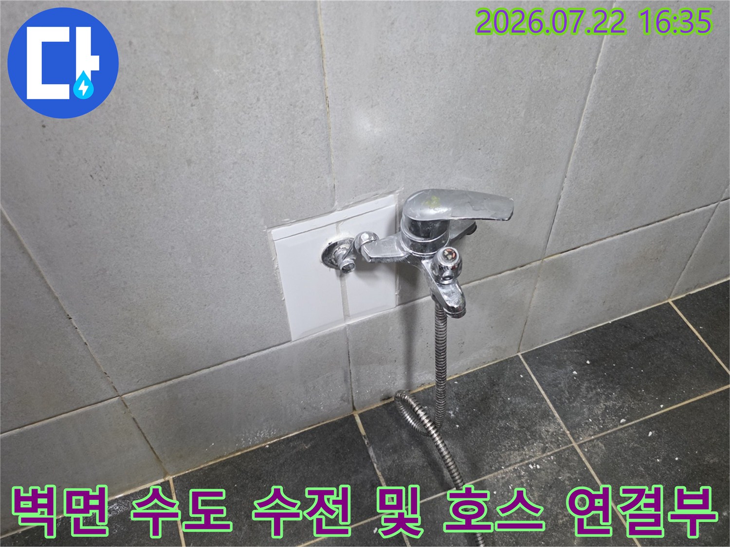 흰색 타일 벽에 고정된 은색 수도꼭지와 아래로 늘어진 금속 소재의 샤워 호스