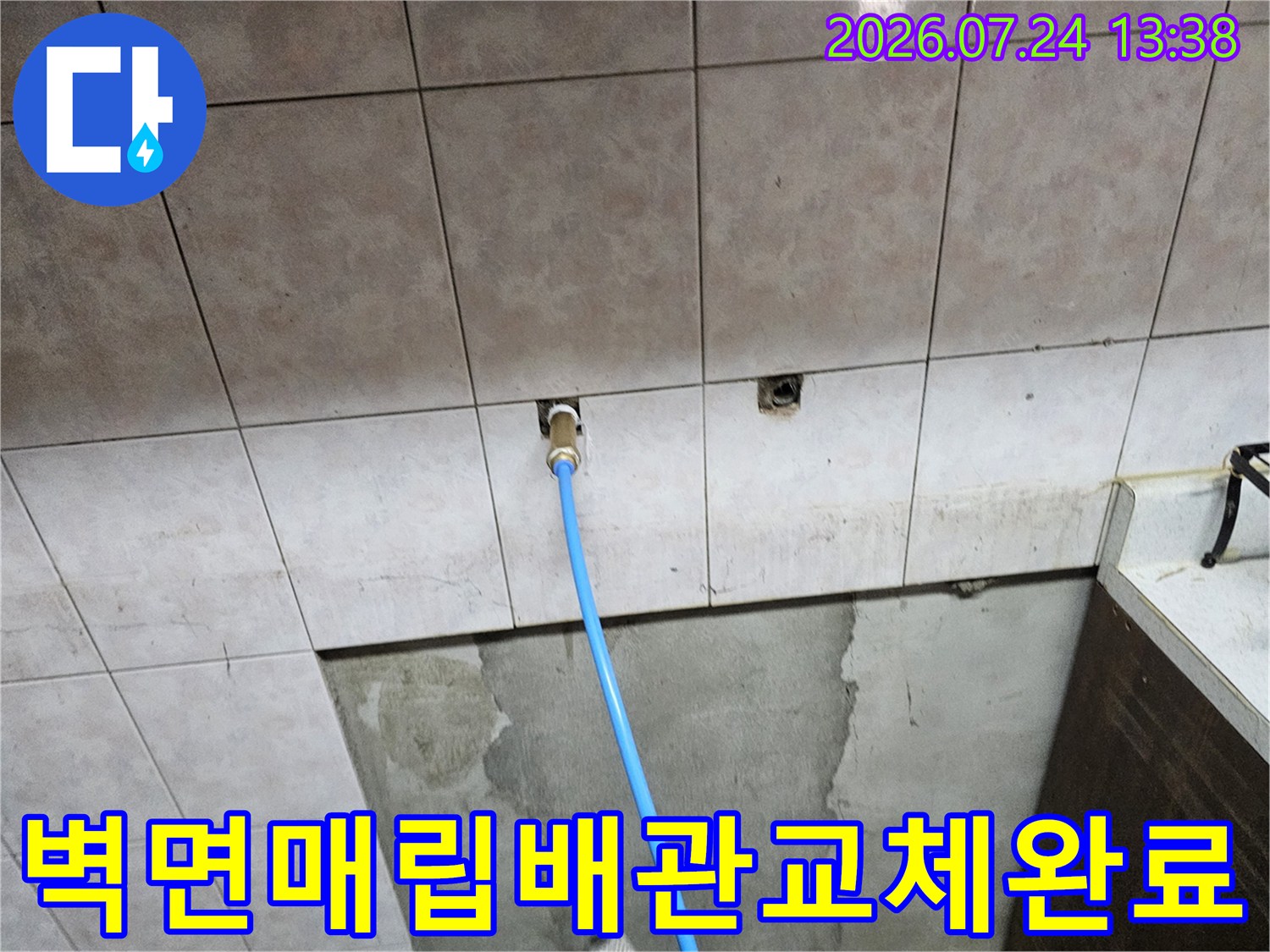 타일 벽 속에서 파란색 신규 배관이 밖으로 연결되어 있는 모습