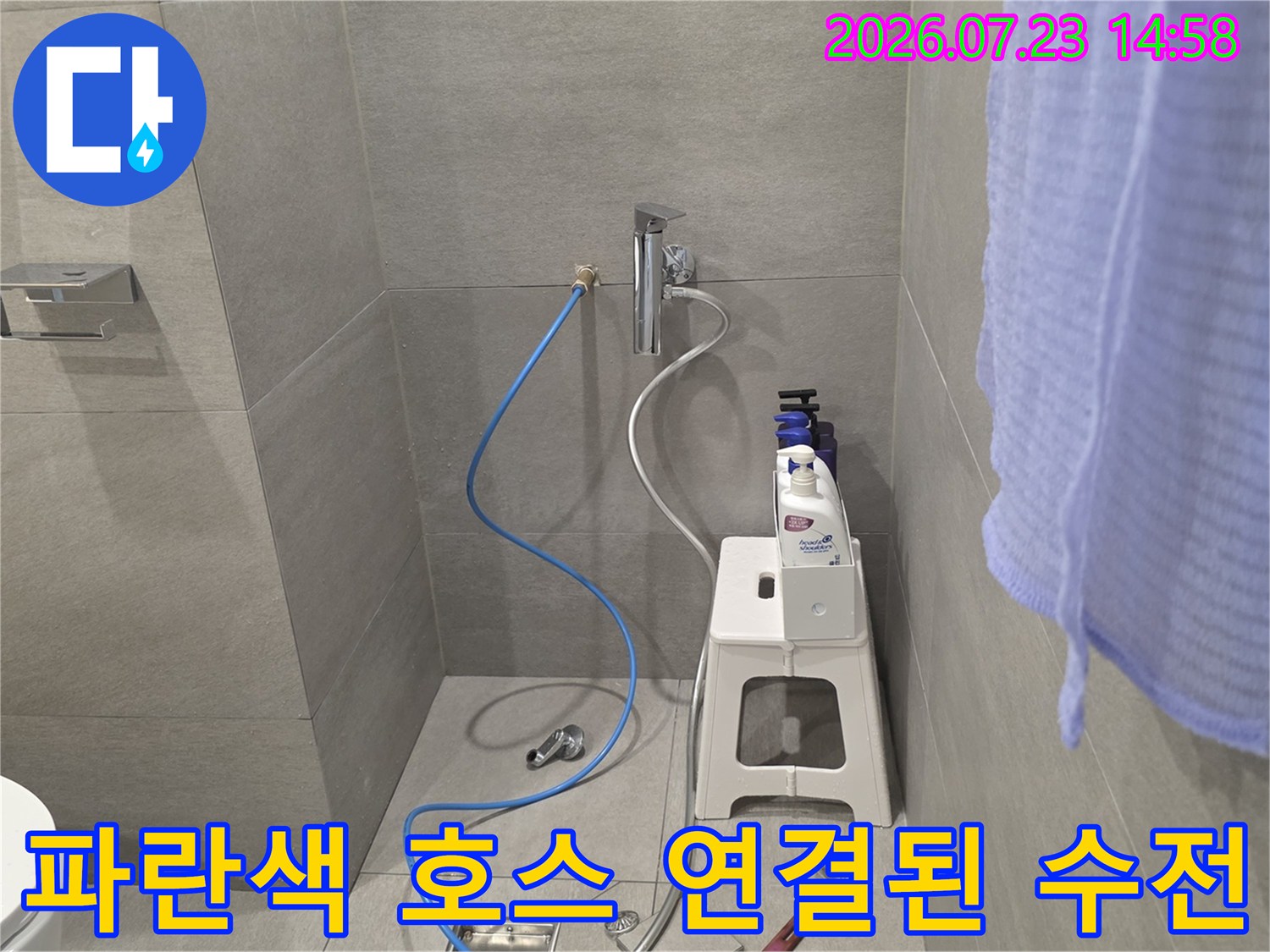 화장실 벽면 수도꼭지에 파란색 호스가 연결되어 바닥으로 내려온 모습