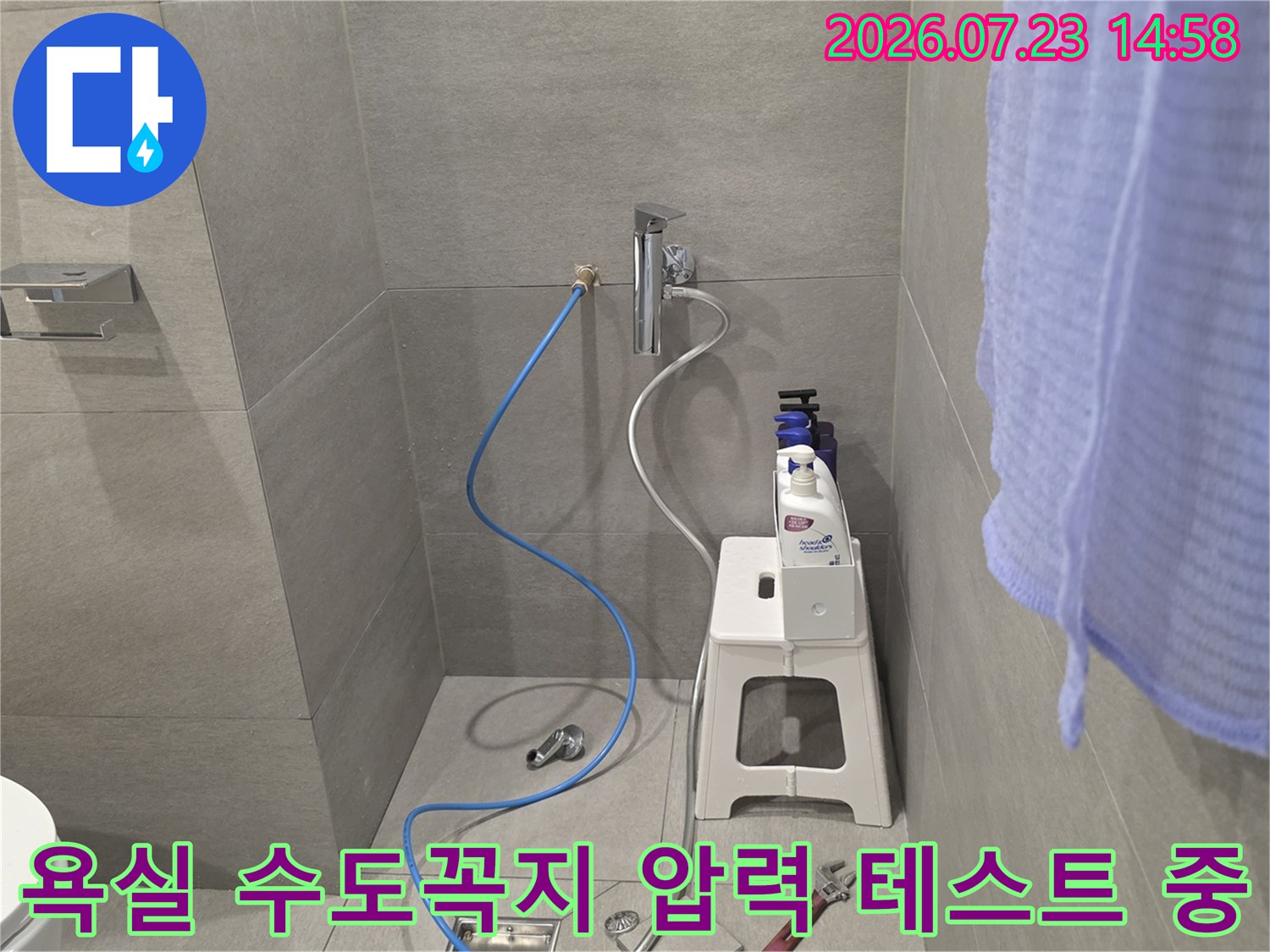 흰색 타일 벽면의 수전에 연결된 파란색 검사 호스와 작업 도구들
