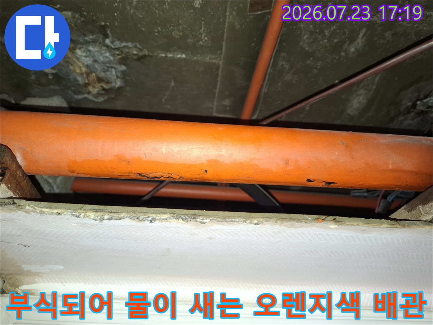 천장에 설치된 오렌지색 배관의 외벽이 부식되어 손상된 모습