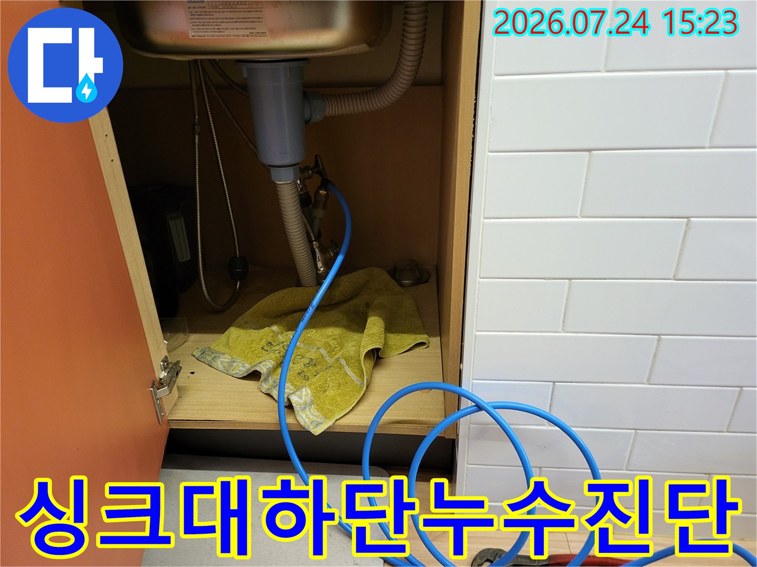 주방 싱크대 아래쪽으로 파란색 테스트 호스가 길게 연결되어 배관 점검을 수행하는 모습