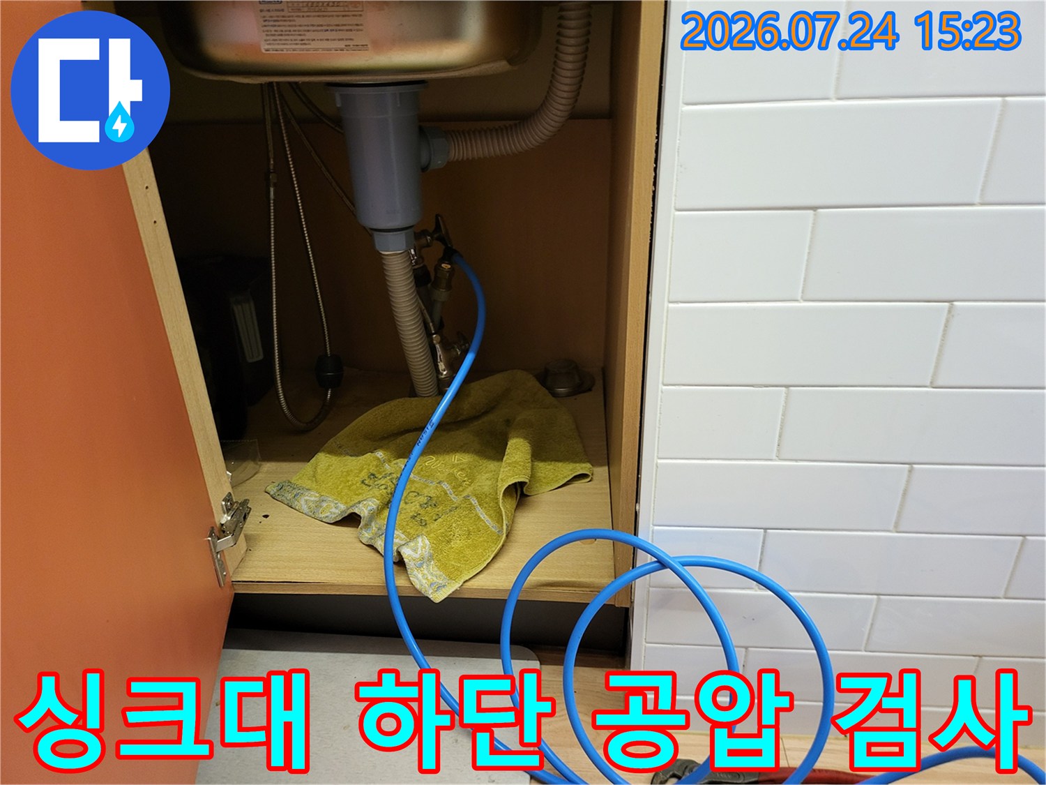주방 싱크대 하부장에서 파란색 공압 호스를 연결하여 누수 여부를 정밀하게 진단하는 모습