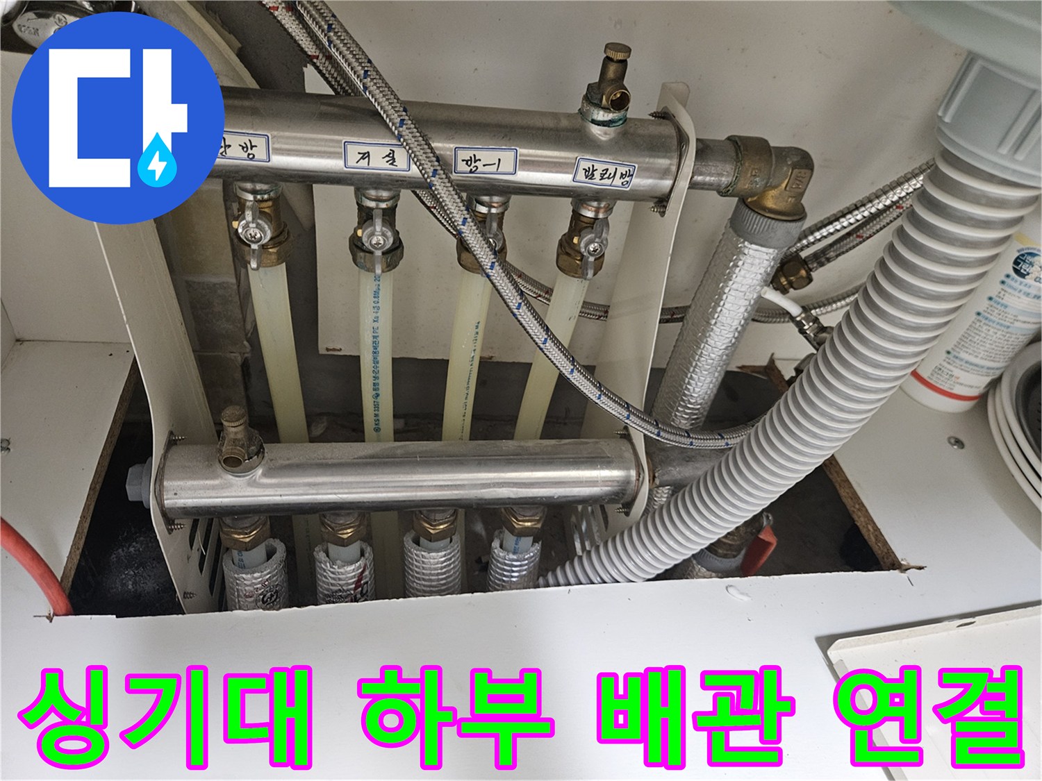 금속 관과 굵은 주름관이 함께 설치된 싱크대 하부 모습