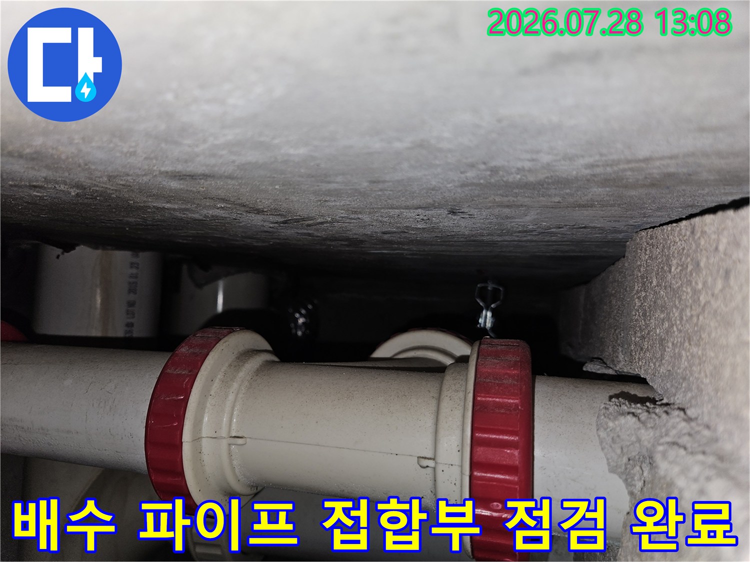 주방 하부 공간의 좁은 구석에 위치한 배출용 파이프 연결부를 촬영한 사진