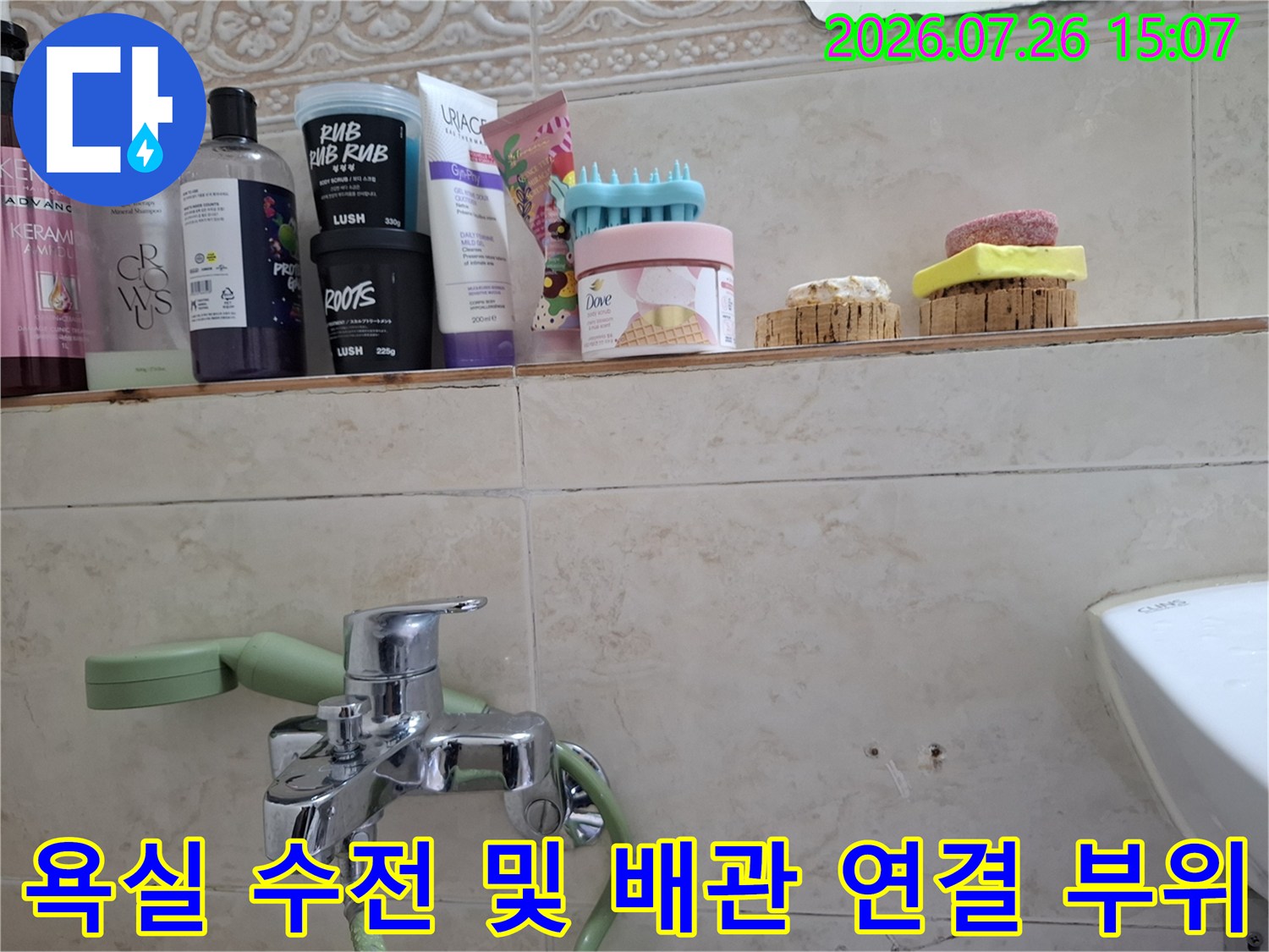 은색 금속 수전과 초록색 유연한 호스가 벽면 타일에 고정된 모습