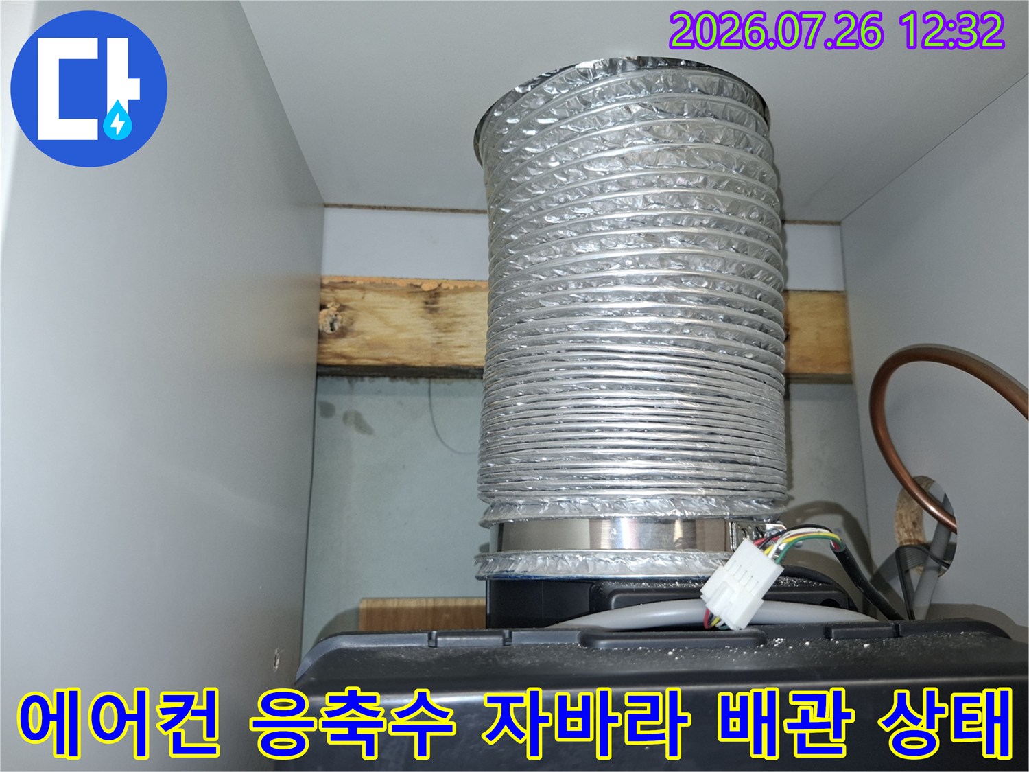 천장 구조물 아래 설치된 은색의 주름진 에어컨 배출관과 하단 기기 연결 부위-정면 사진
