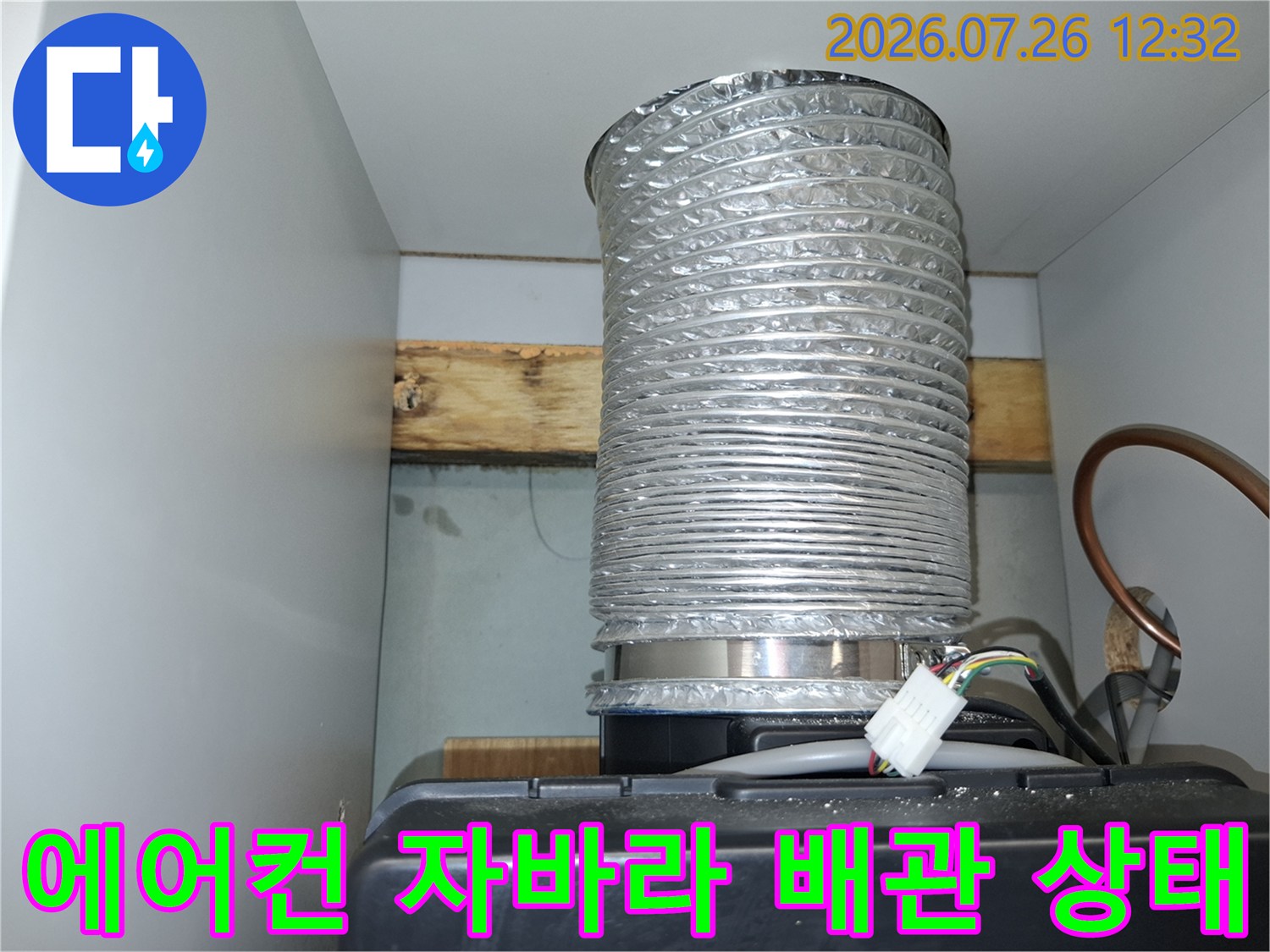 천장에 연결된 은색의 주름진 에어컨 배관과 구리관-전선 뭉치가 보이는 모습