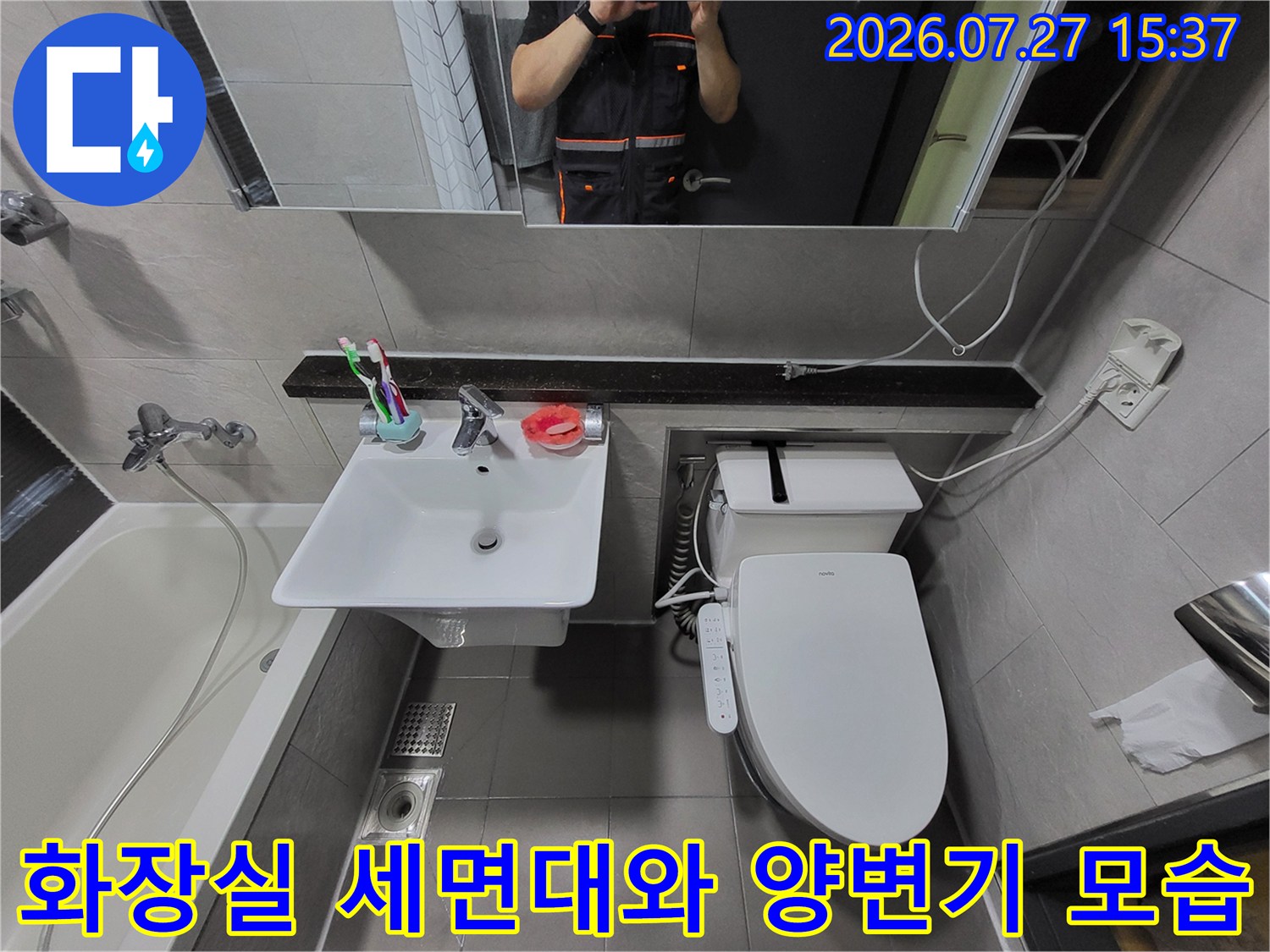 흰색 세면대와 변기가 설치된 화장실 내부-거울에 비친 작업자의 모습