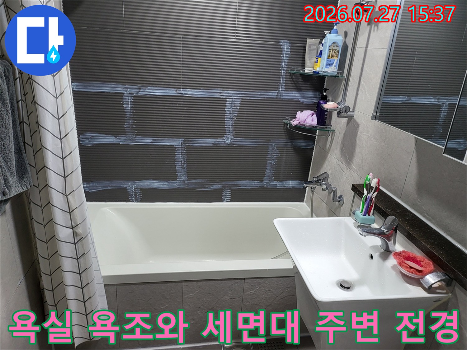 흰색 욕조와 세면대가 설치되어 있고 벽면에 회색 타일이 시공된 화장실 내부 모습