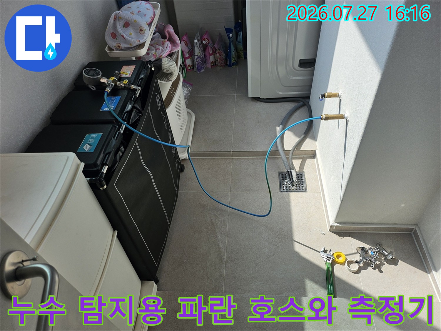 타일 바닥 위에 놓인 누수 점검 장비와 벽면의 급수 밸브에 연결된 파란색 배관 라인