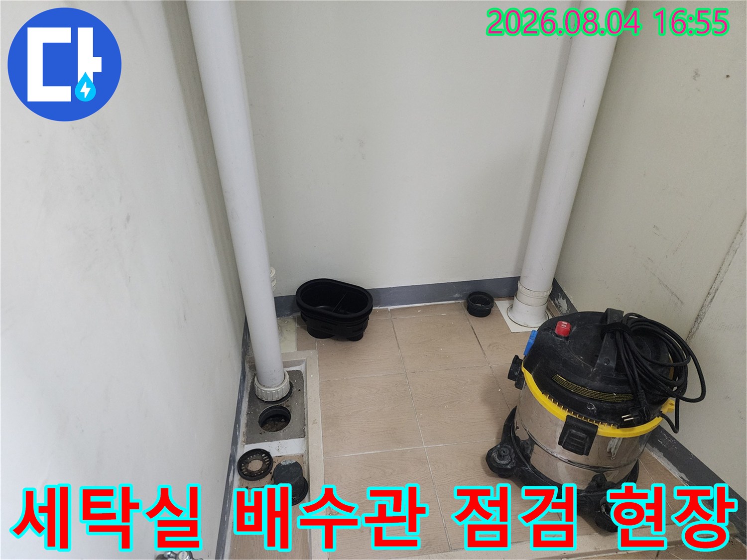 세탁실 바닥의 노출된 배수 트랩과 청소 장비가 놓인 공사 현장
