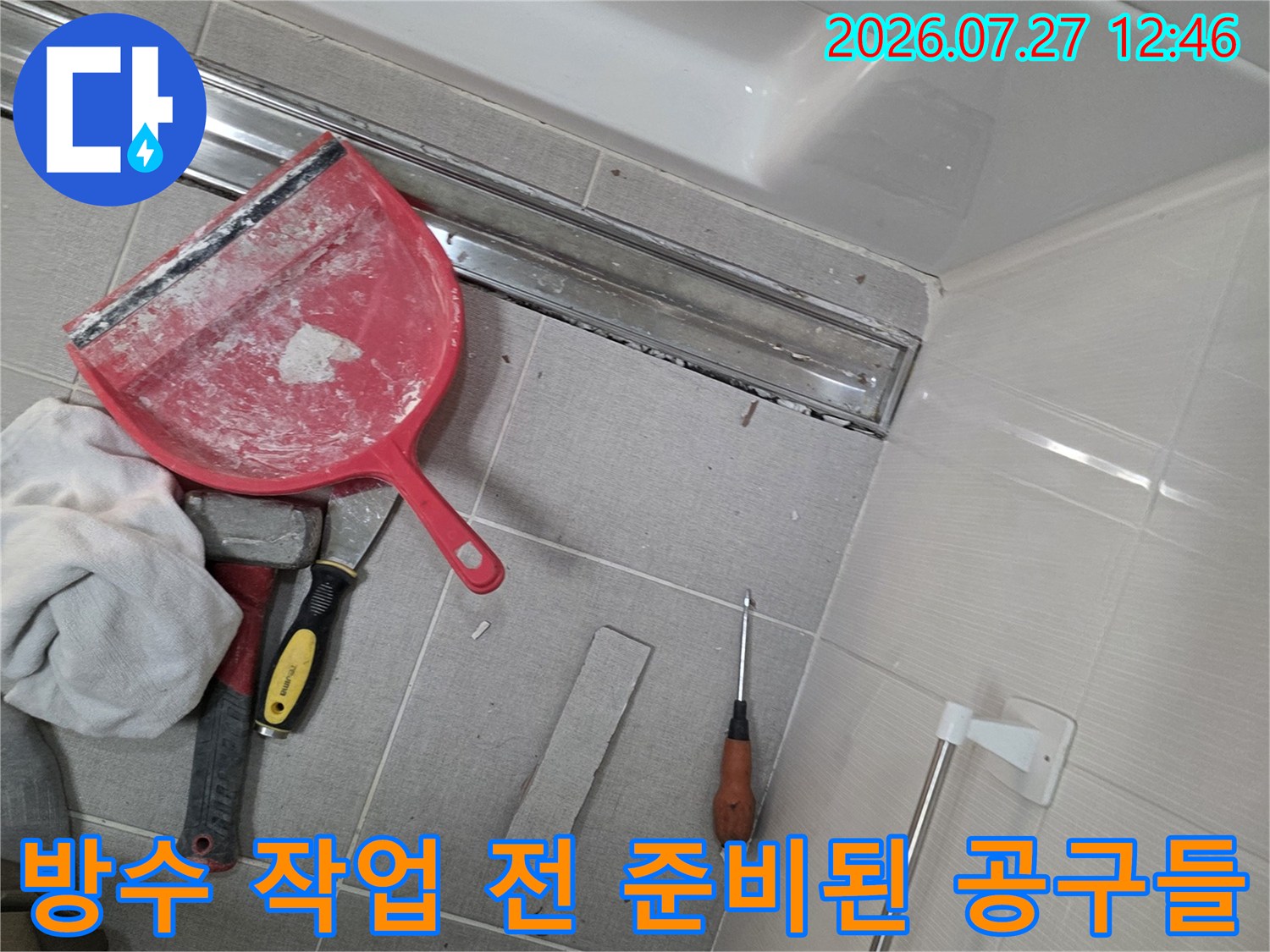 화장실 바닥 트랜치-배수구 옆에 놓인 빨간색 밀대형 헤라와 작업용 장갑과 도구들