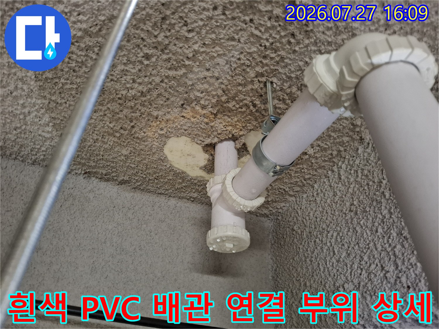 거친 콘크리트 천장에 설치된 흰색 PVC 하수관-티자형 소켓과 금속 고정 장치