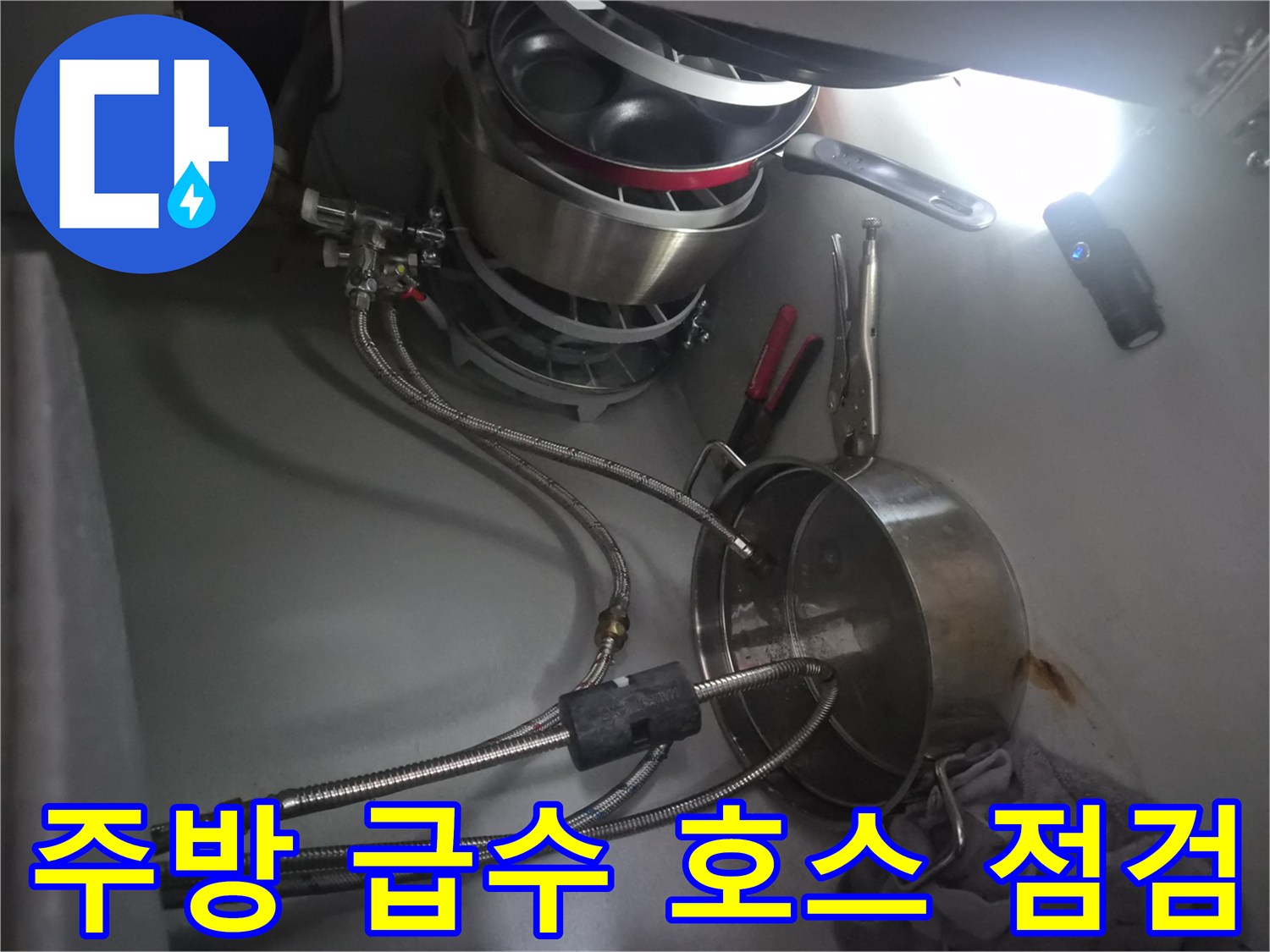 금속 재질의 굴곡진 배관과 연결 부품이 보이는 싱크대 하부 모습