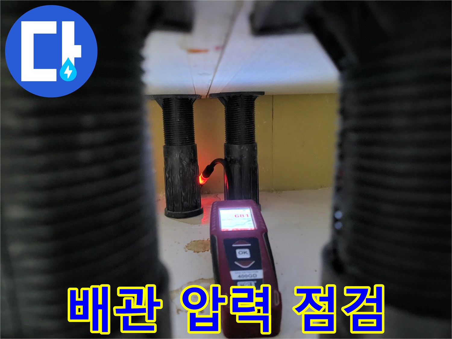 검정색 수직 배관 근처에 놓인 휴대용 가스 탐지기 장비