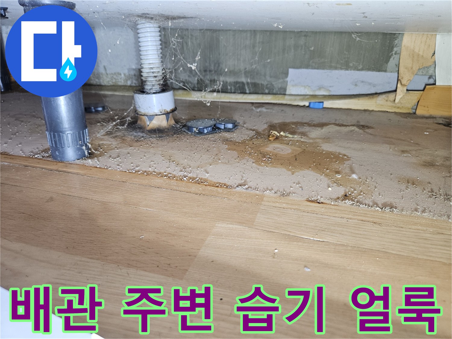 싱크대 아래쪽 배관 연결 부위의 젖은 흔적과 오염된 나무판