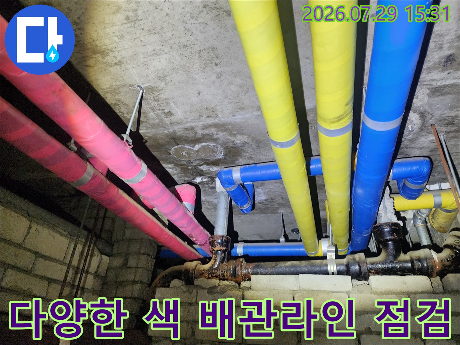 천장에 설치된 분홍색과 노란색 보온재를 씌운 배관들의 모습입니다.