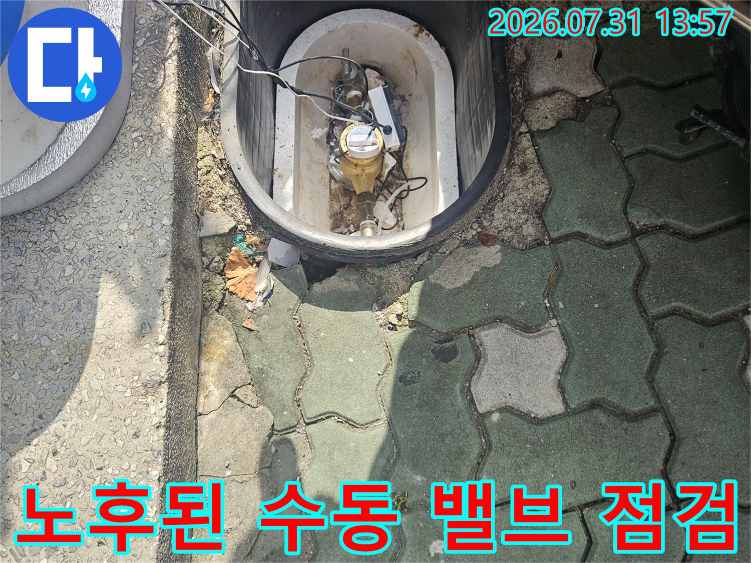 먼지 쌓인 맨홀 내부에서 수도 계량기와 배관 연결부를 촬영한 모습