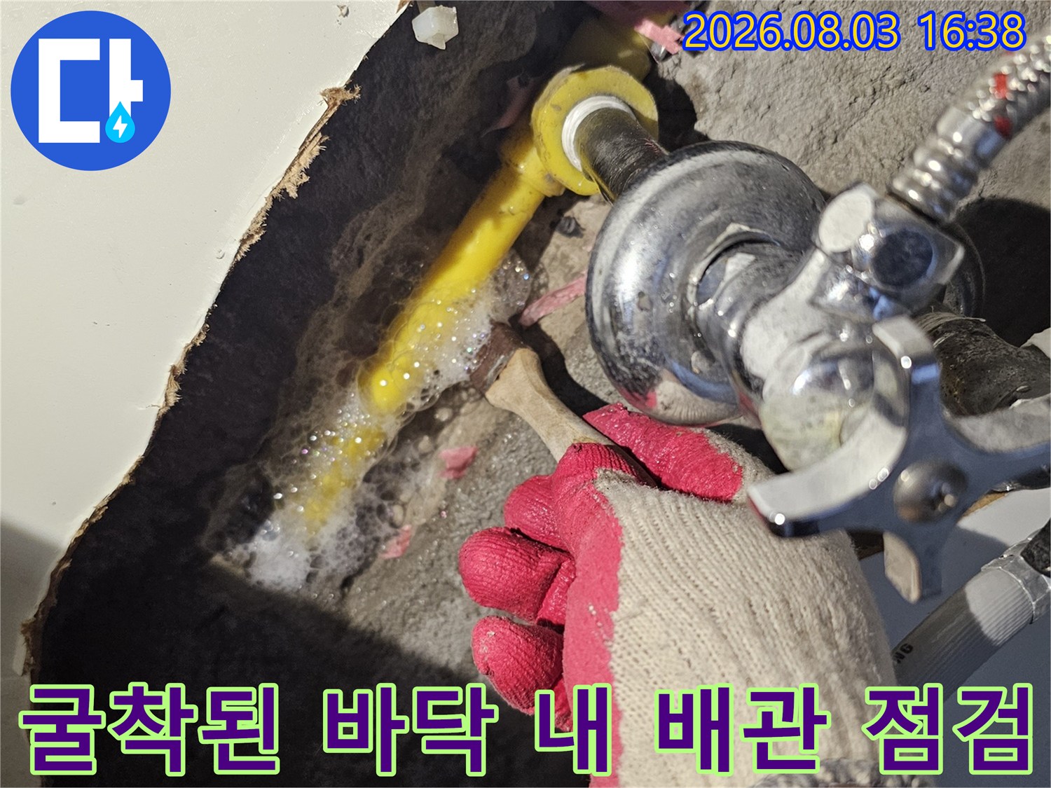 싱크대 아래 파헤쳐진 공간 속 노란색과 회색이 섞인 배관 부위를 살피는 장면
