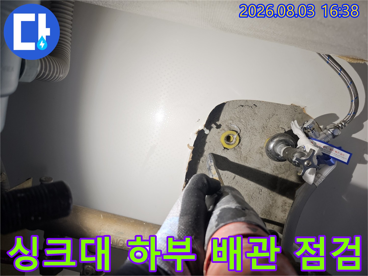 작업자가 싱크대 하부의 노란색 PB 배관과 회색 배관이 섞인 구간을 손으로 세밀하게 검사함