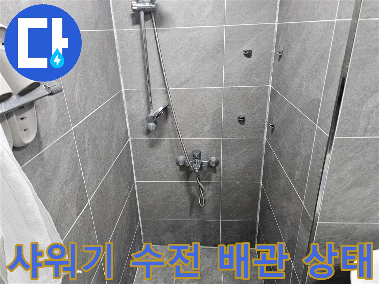 회색 타일 벽면에 설치된 샤워기 조절 밸브 및 호스 연결부