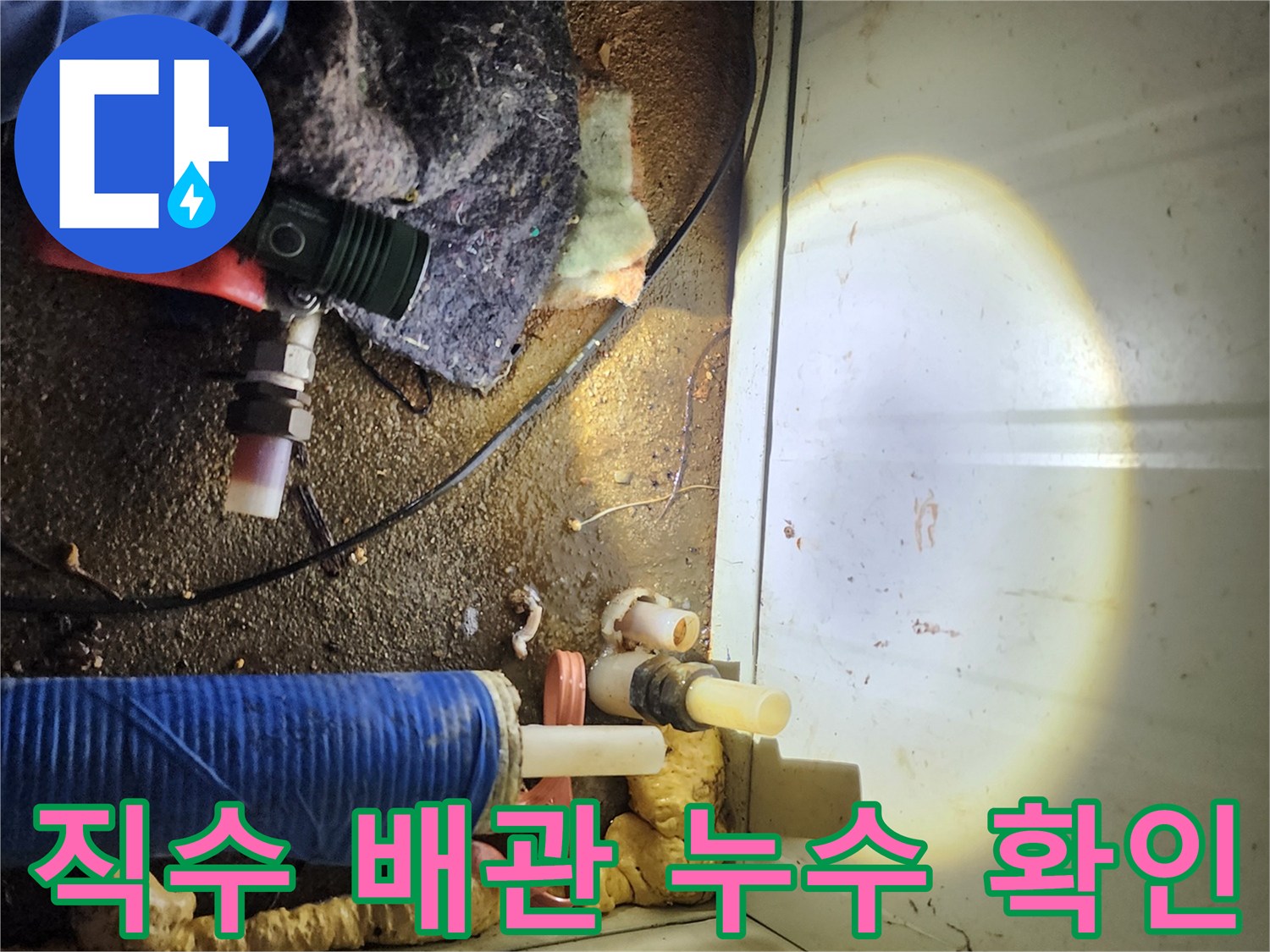 어두운 배관 구석을 조명으로 비추며-누수 부위를 찾는 모습