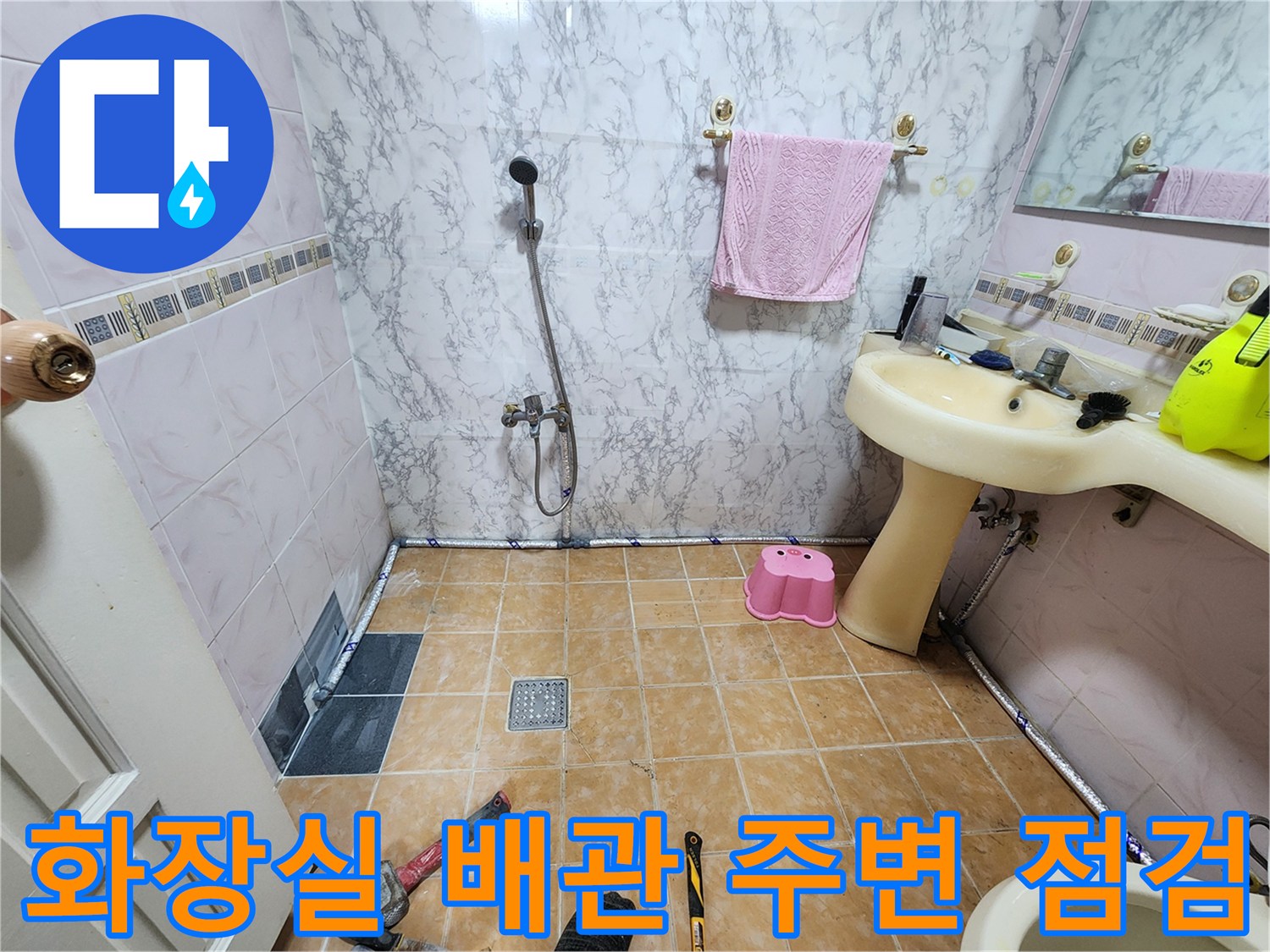 세면대 하단 배관과 바닥 타일의 연결 부위를 면밀히 조사 중인 현장 사진