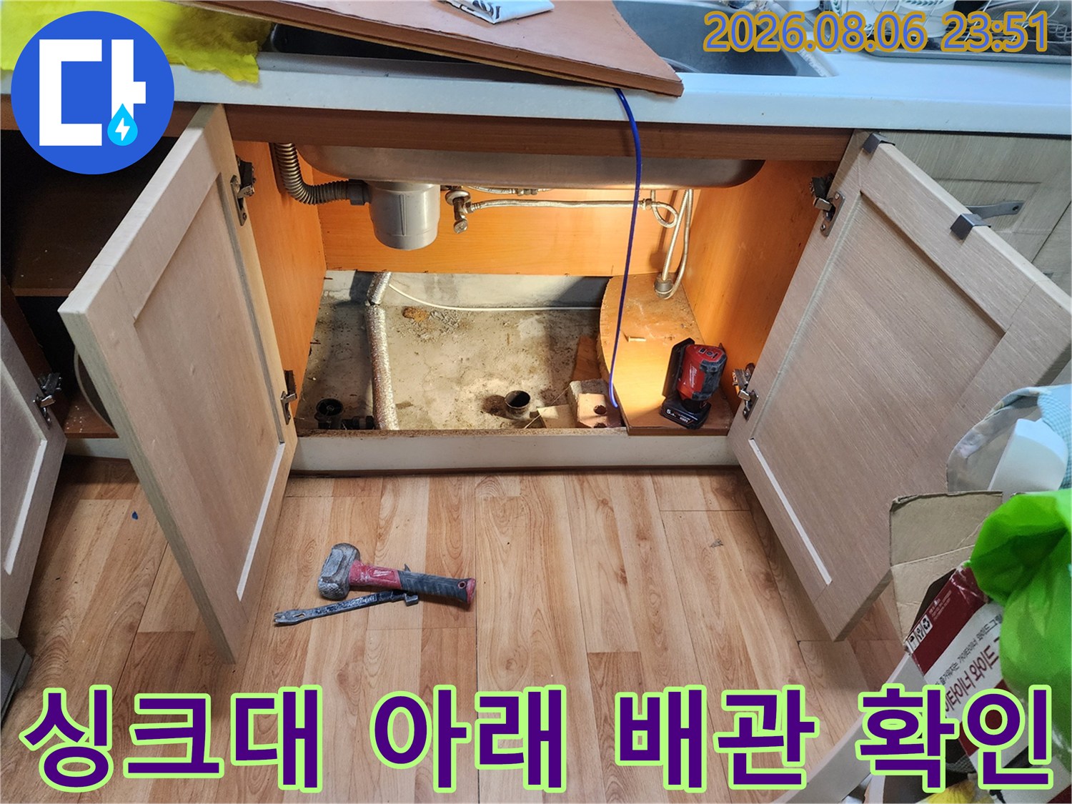 싱크대 밑 하부장 내부의 노출된 배관과 작업 도구들