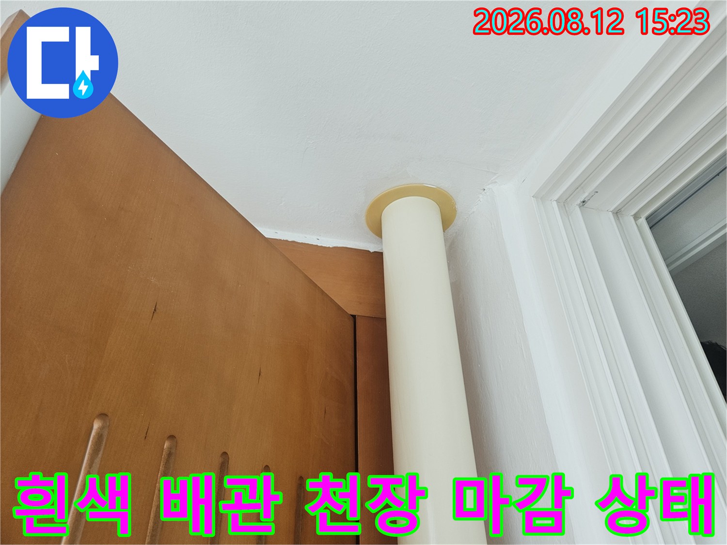 천장 구석에 설치된 흰색 수직 배관과 바닥면의 접합부-마무리 처리 모습
