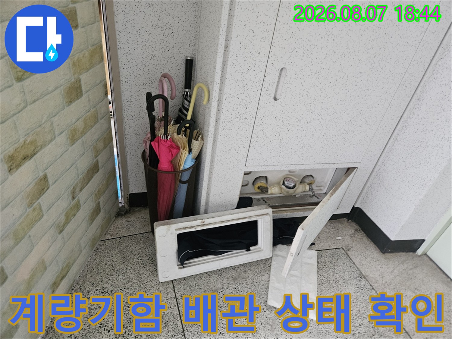 아파트 계량기함을 열어 수도 배관의 연결 부위를 점검하는 현장 사진입니다.