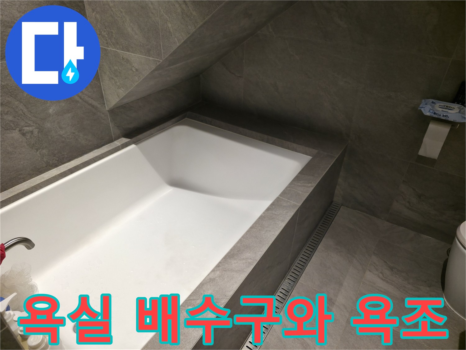 욕조 옆 배수 슬롯과 회색 타일이 시공된 현장 사진입니다.