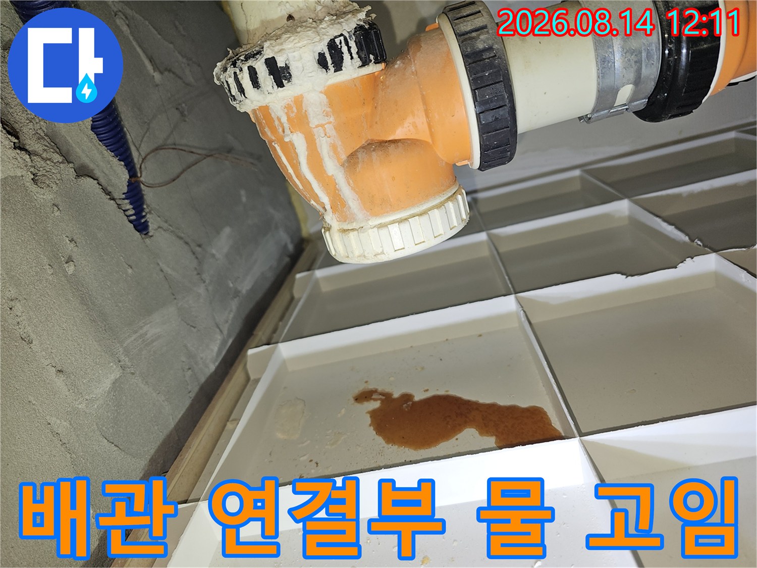 오렌지색 배관 소켓 아래로 형성된 누수 얼룩과 고인 물