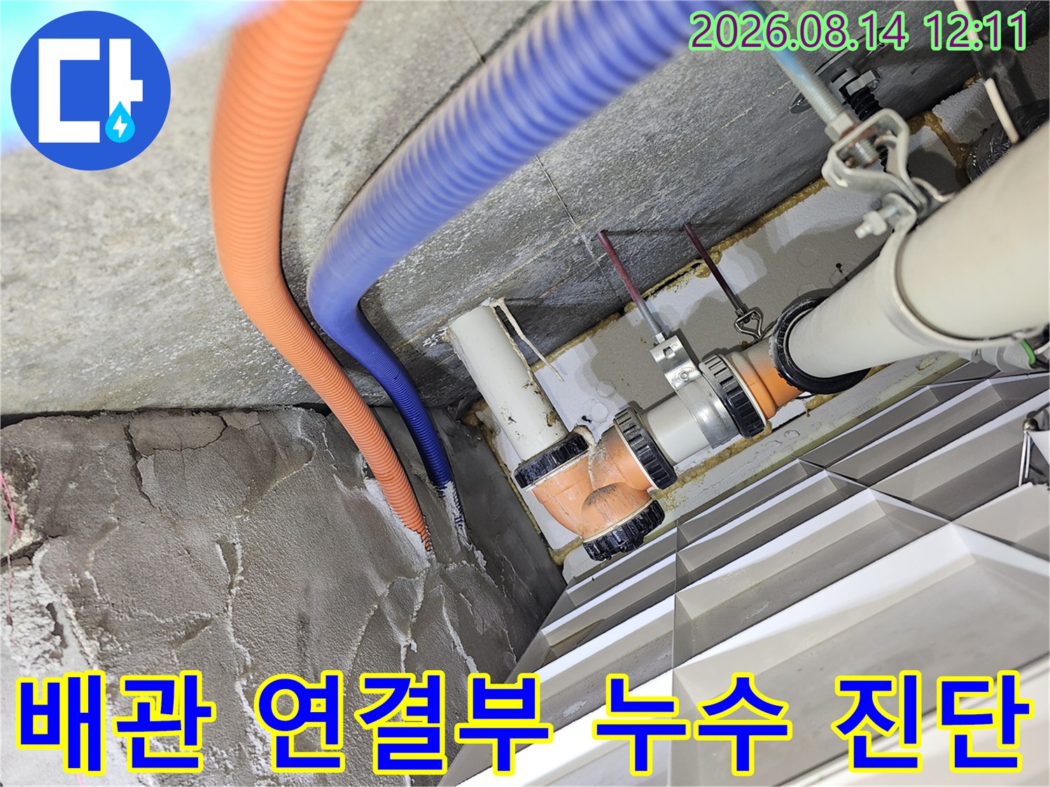 오렌지색 주름관과 파란색 호스가 지나가는 배관 부위를 정밀하게 관찰하는 모습입니다.