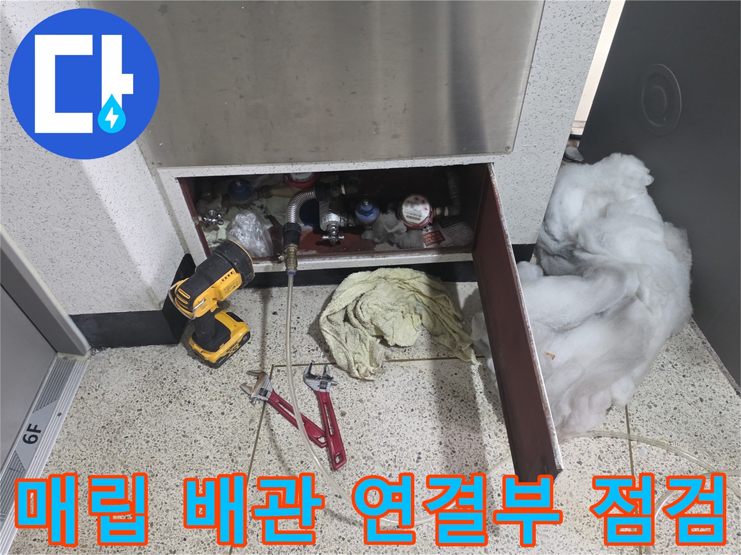 싱크대 하단 내부의 금속 배관들과 작업용 공구가 놓여 있는 현장 사진