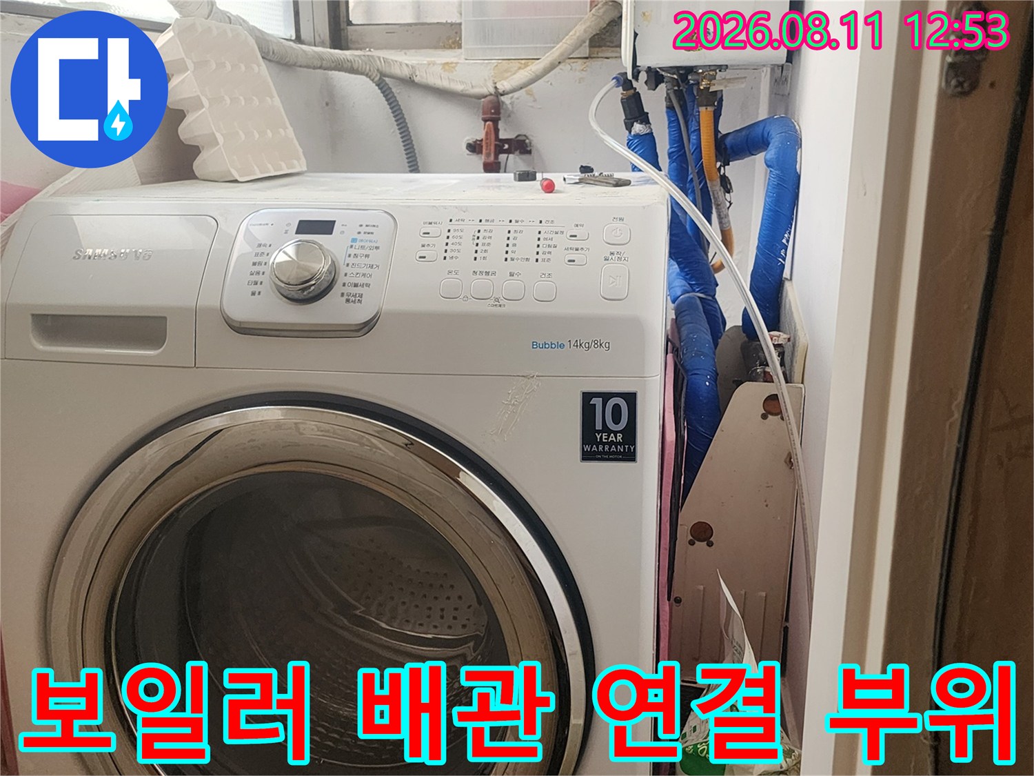 보일러 컨트롤러와 파란색 수도 배관이 복잡하게 얽힌 세탁실 내부 모습입니다.
