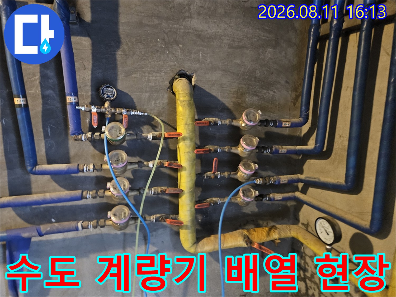 노란색 메인 관과 파란색 보온재 배관들이 연결된 수도 계량기 모습입니다.