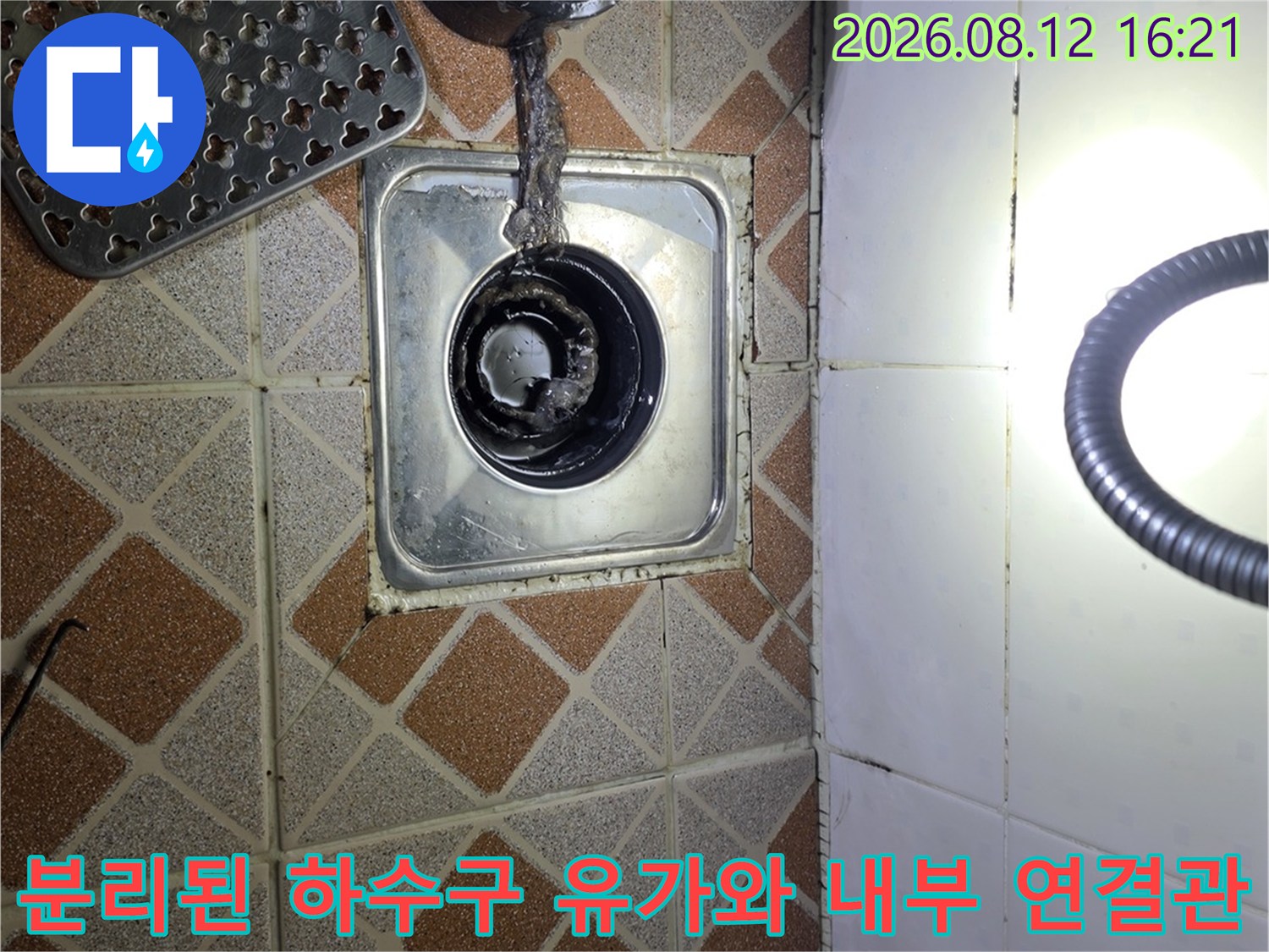 욕실 타일 바닥에 설치된 스테인리스 유가-내부의 오염된 배관 연결부가 드러난 사진