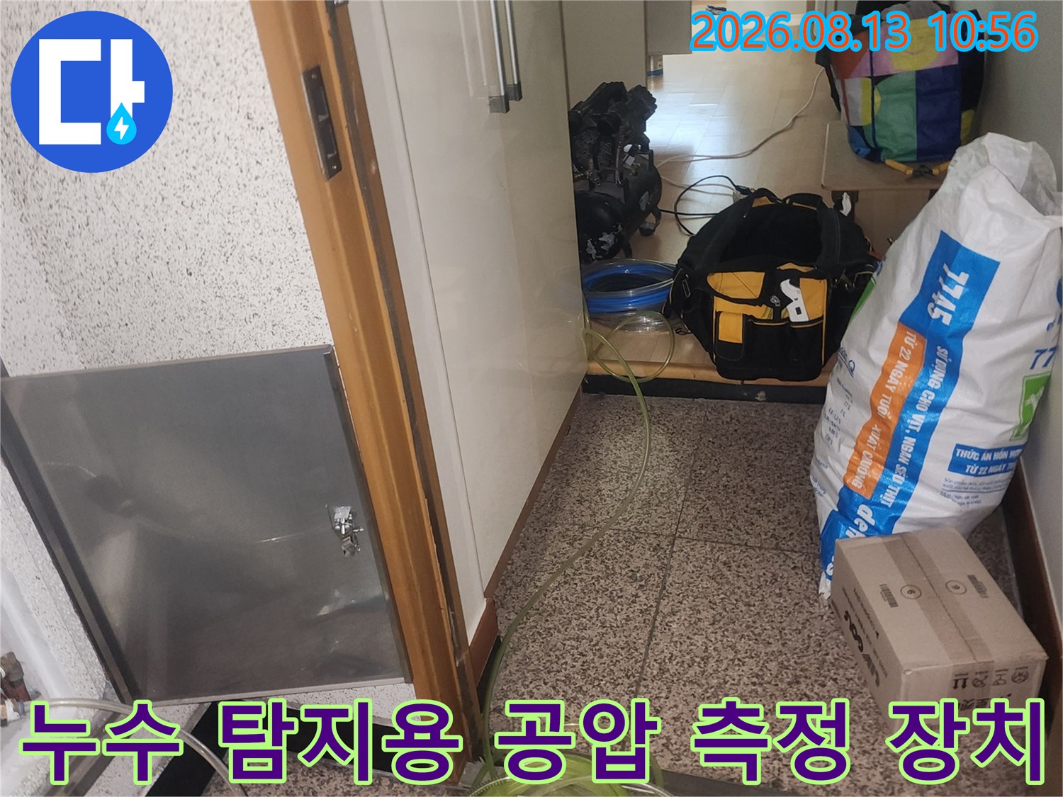 스텐 점검구 틈으로 연결된 노란색 배관 호스와 압력 게이지-누수 진단 장면