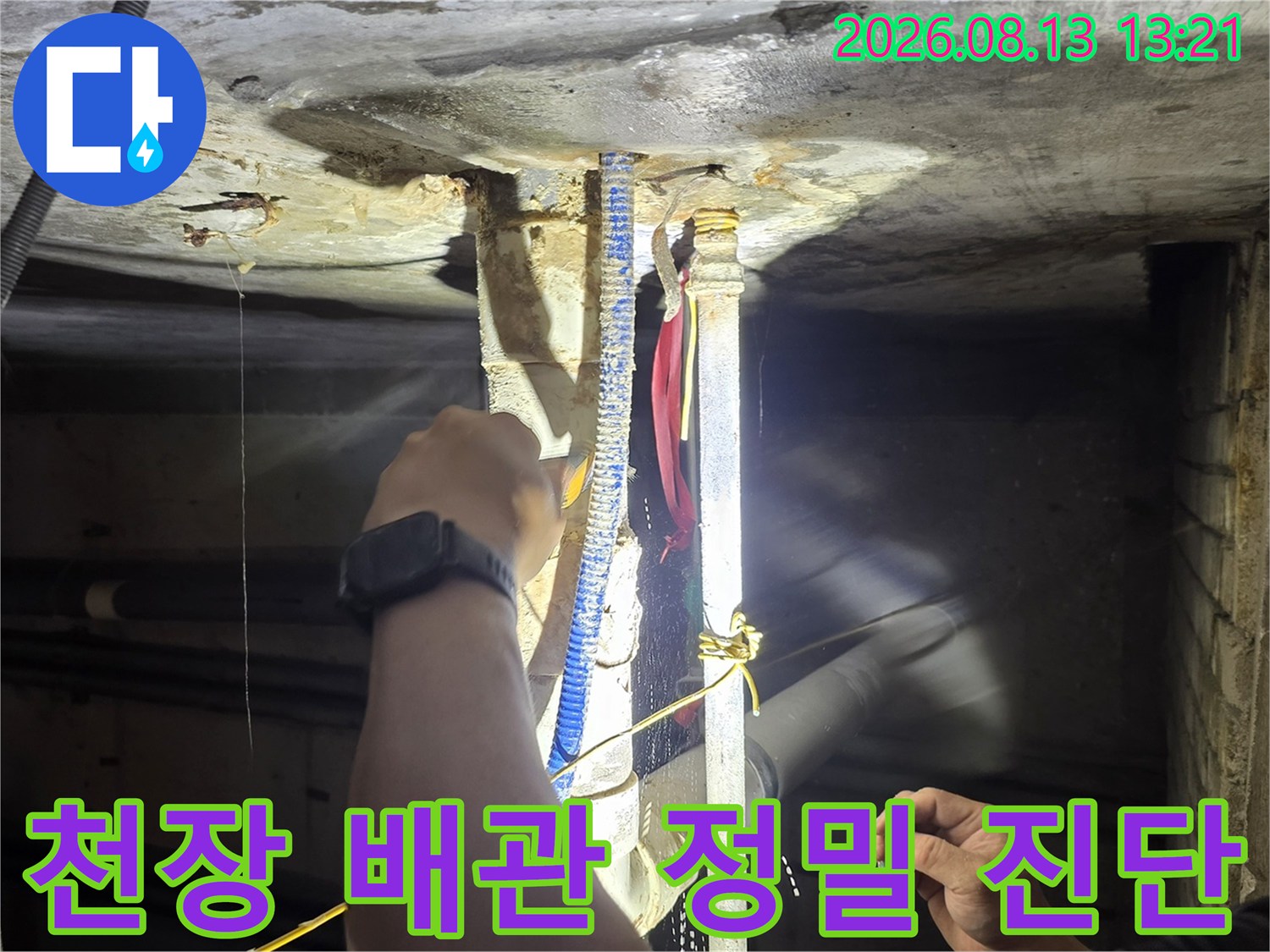 손전등으로 천장 슬래브 아래 배관의 결함을 찾는 작업 장면입니다.