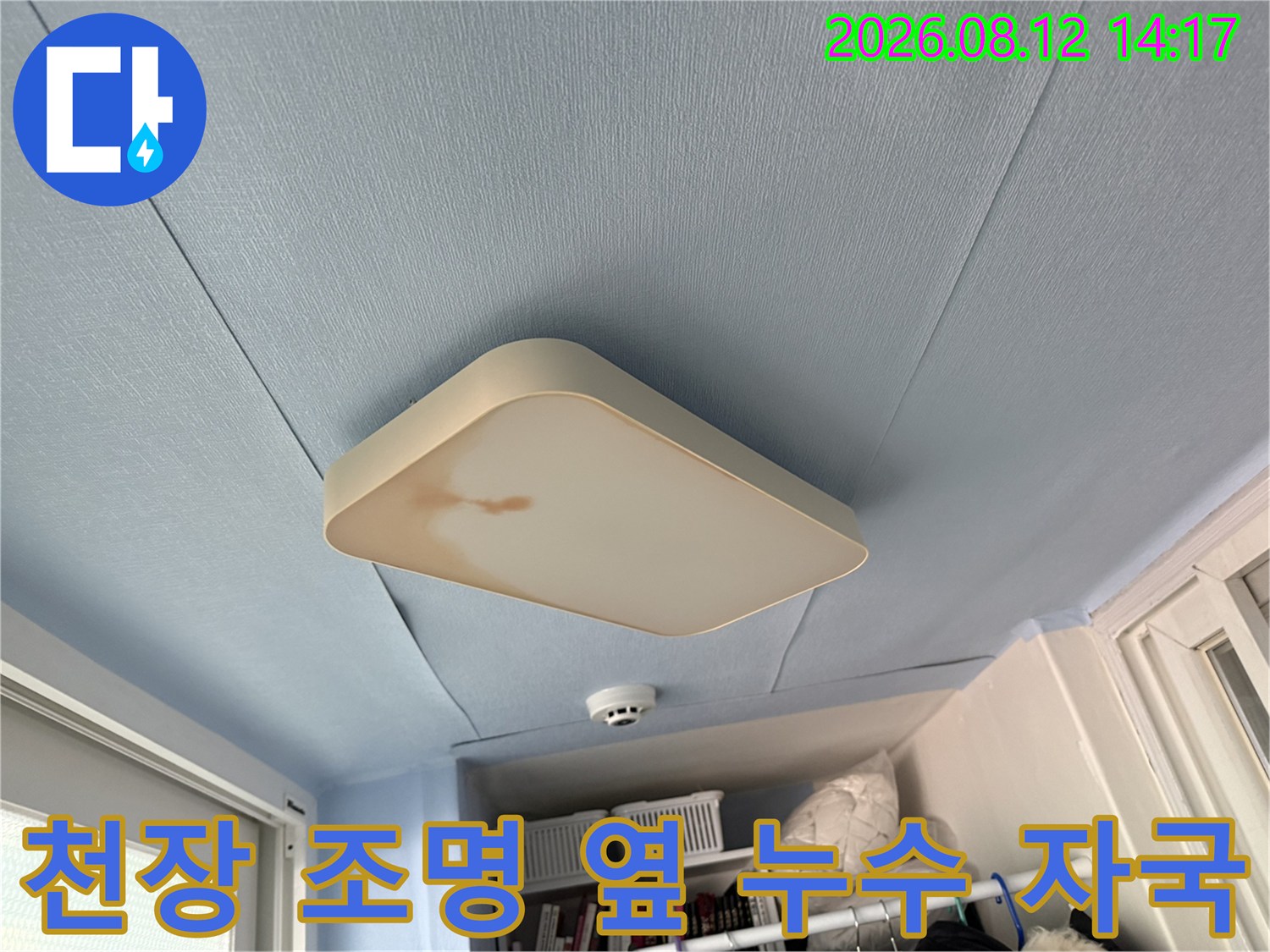 푸른색 천장 배경에 설치된 사각 전등 주변의 갈색 누수 오염 부위