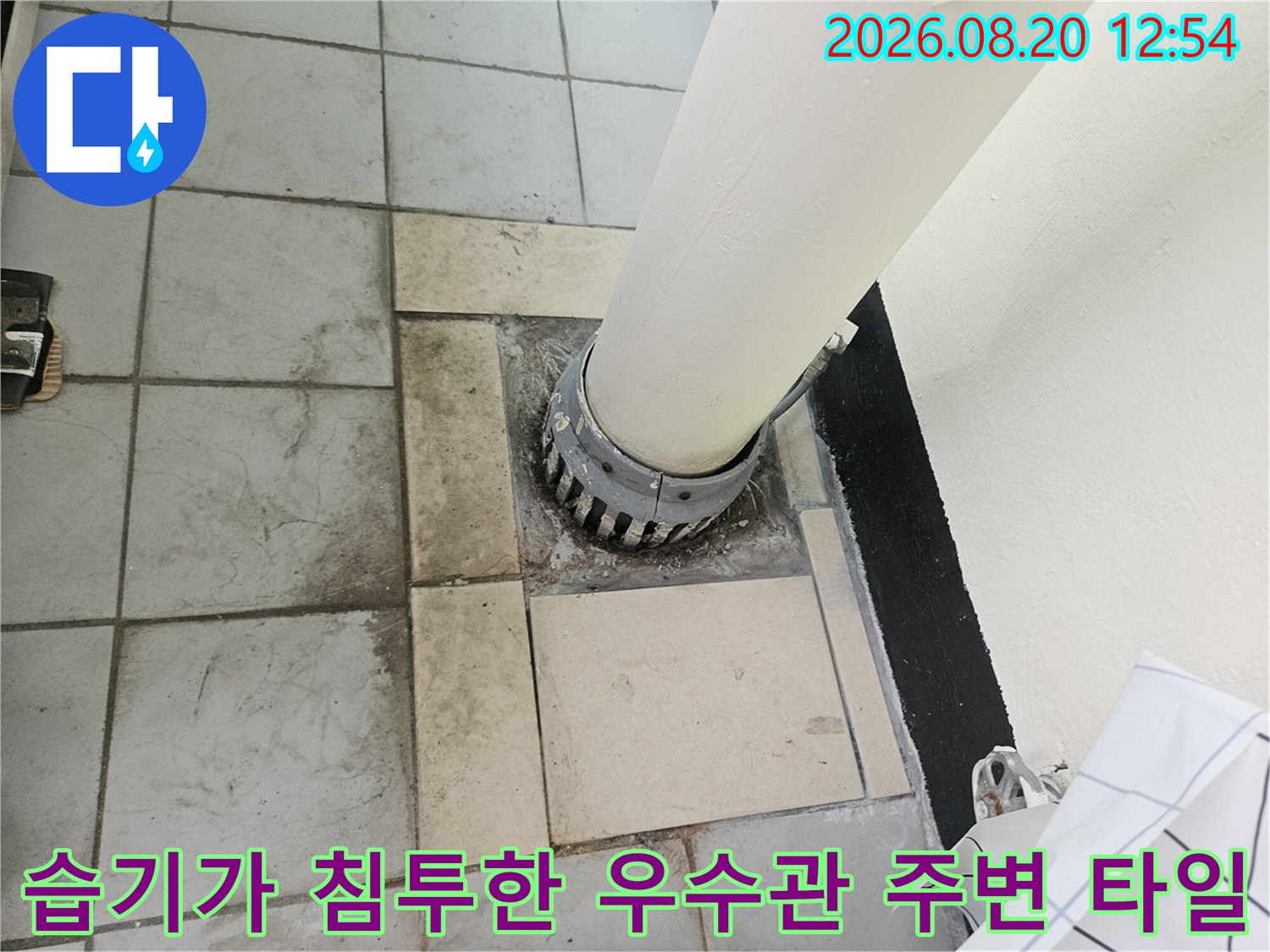 우수관 배관 주위의 젖은 타일과 오염 상태를 보여줍니다.
