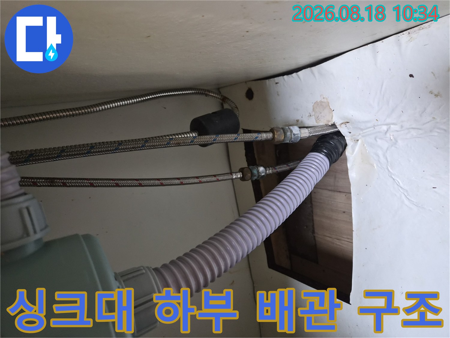 은색 고압 호스와 흰색 주름 배수 호스가 복잡하게 연결된 싱크대 내부