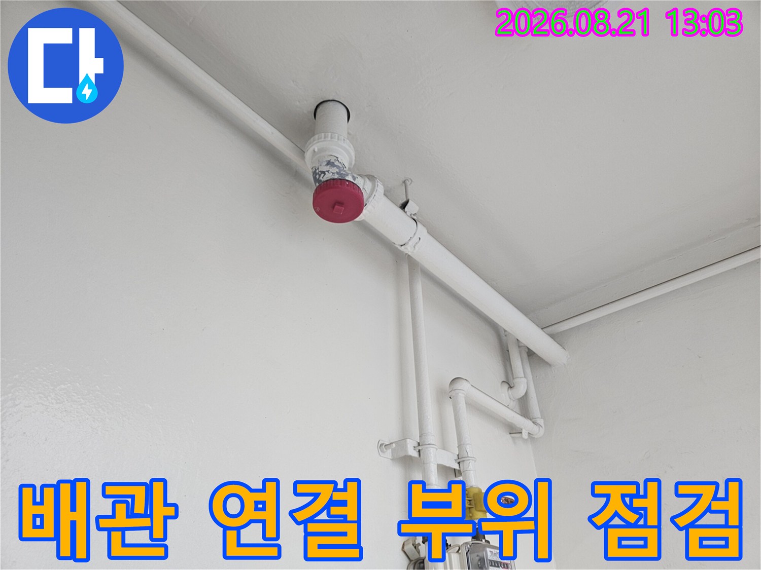 벽면 배관과 수도 계량기가 설치된 싱크대 하부 공간의 모습입니다.