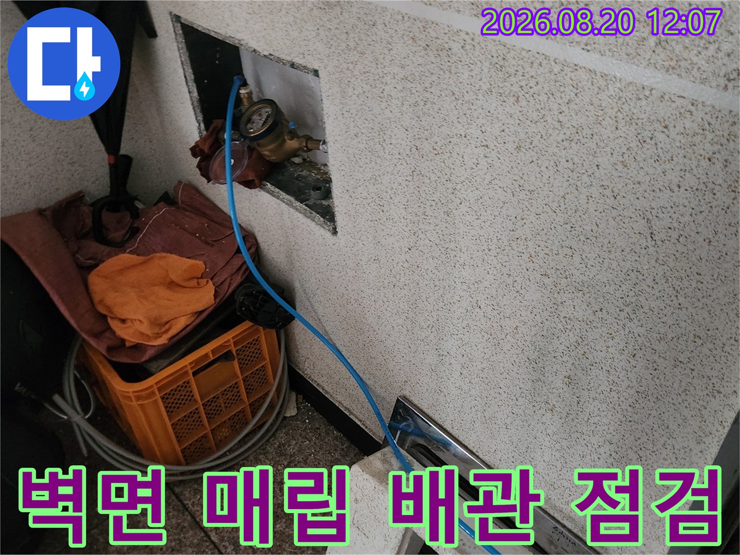 타일 벽 속에 위치한 수도 계량기와 연결된 호스의 모습입니다.
