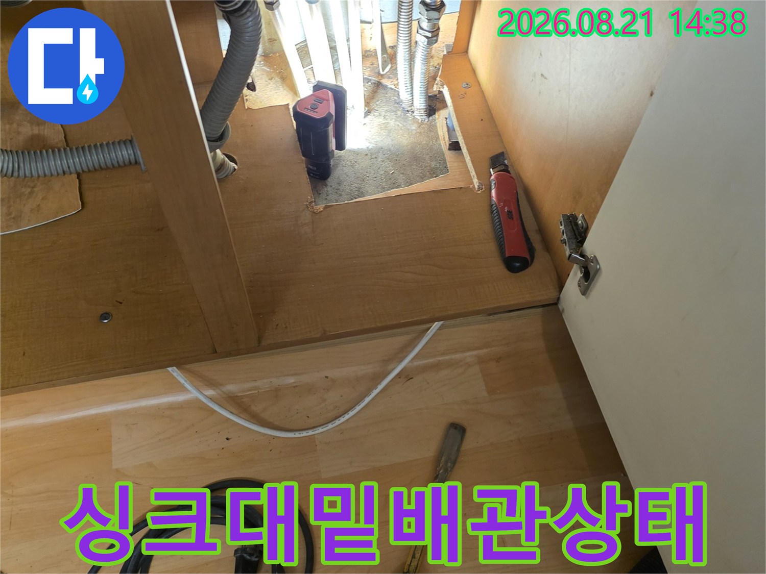 싱크대 밑에 노출된 여러 개의 배관과 점검용 장비가 보이는 사진입니다.