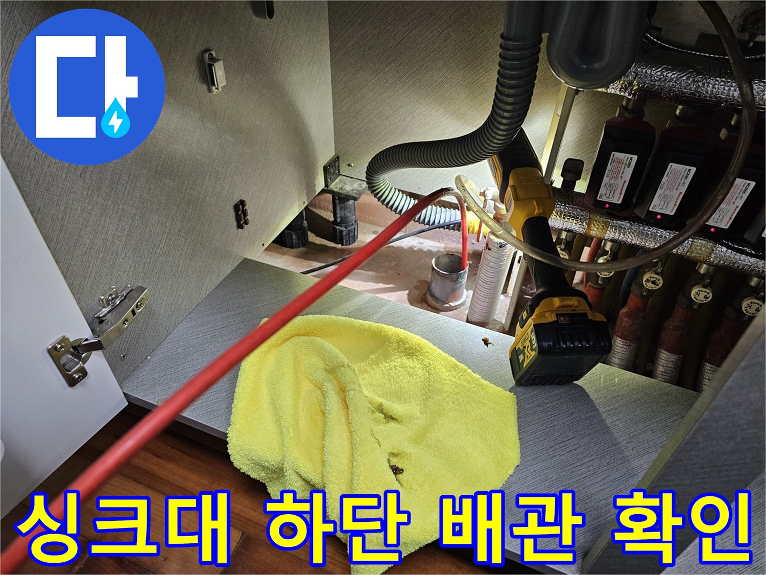 싱크대 아래 분배기 부근의 배관들을 면밀히 조사하는 현장 사진입니다.