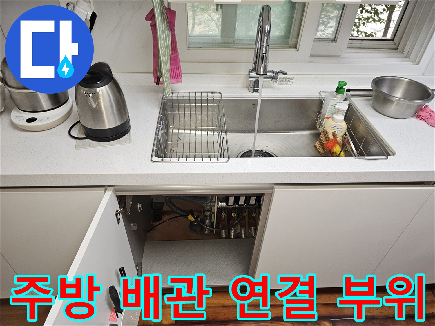싱크대 하부 수납장 내부의 복잡한 수도 배관과 분배기 모습